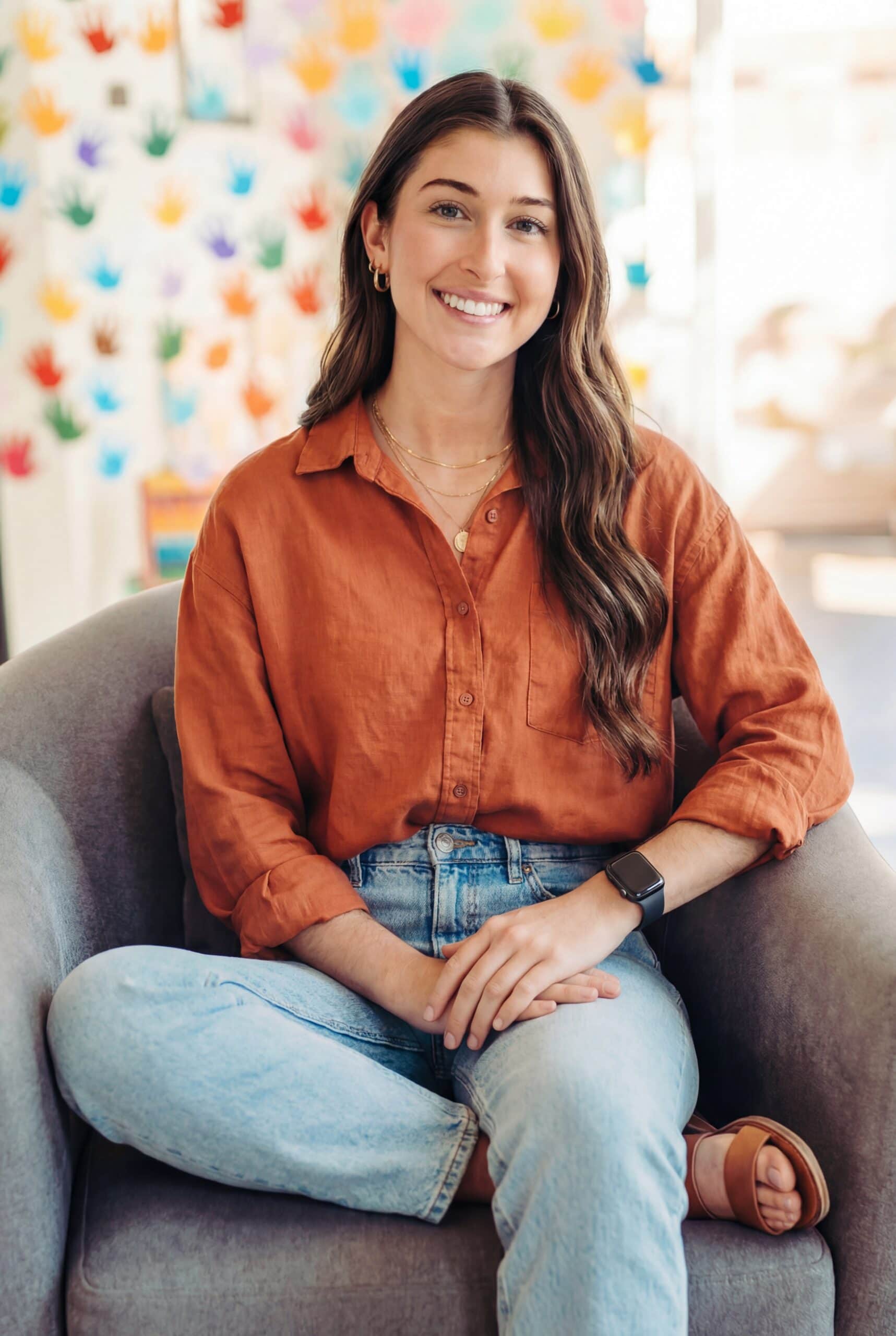 Dr. Antonia Denison smiling in the River City Wellness office with colorful children's handprints in background South Austin pediatric chiropractor